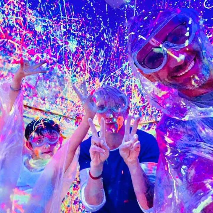 a dad and 2 kids smiling for the camera with goggles on in the splatter room
