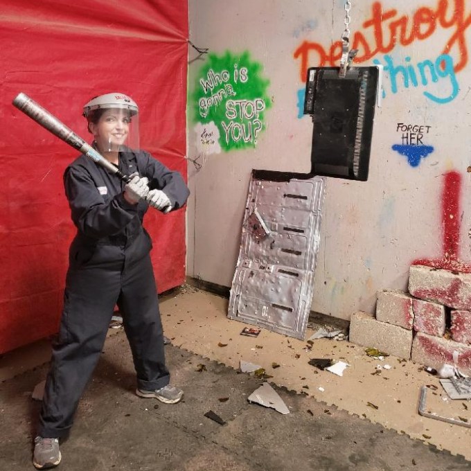 a women holding a bat that is going to hit the hanging electronic in the rage room