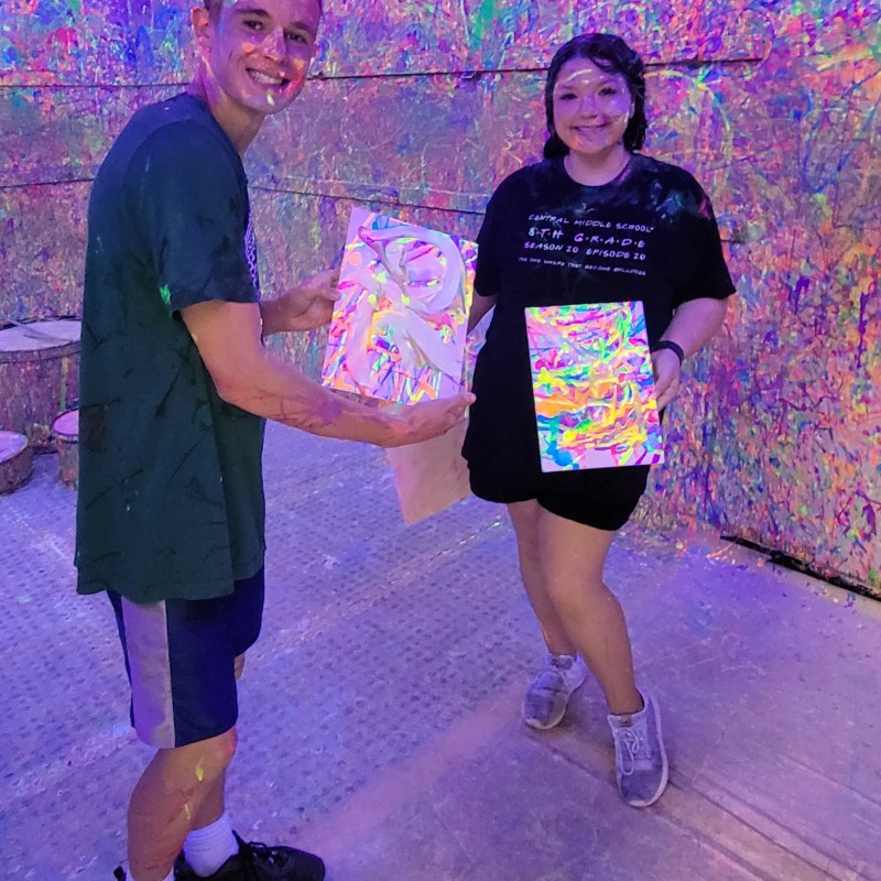 a man and woman posing with the canvases they painted inside of the splatter room