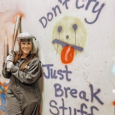 a person holding a bat in front of a wall sign in the rage room