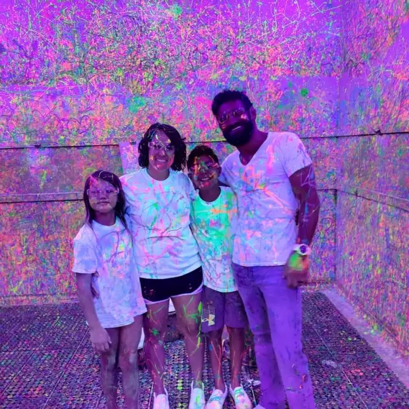 a family of 4 posing inside of the splatter paint room at chaos factory