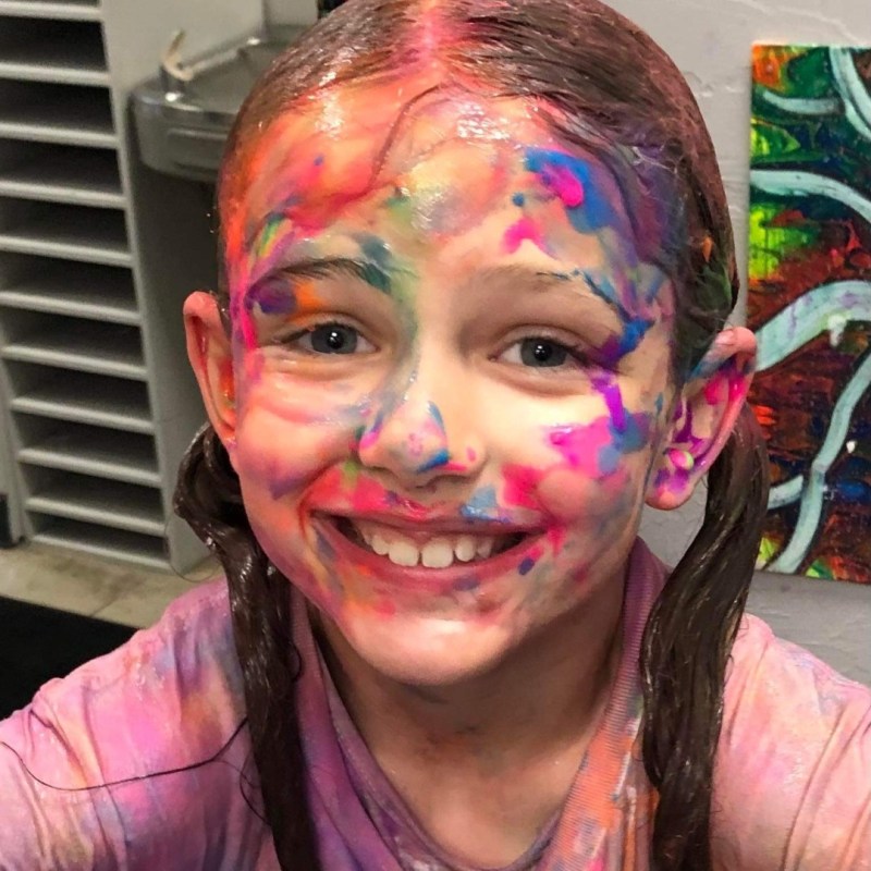 a smiling girl taking a selfie with paint all over her face