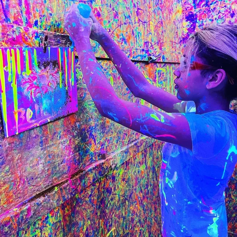 a young lady putting paint on her canvas in the splatter paint room