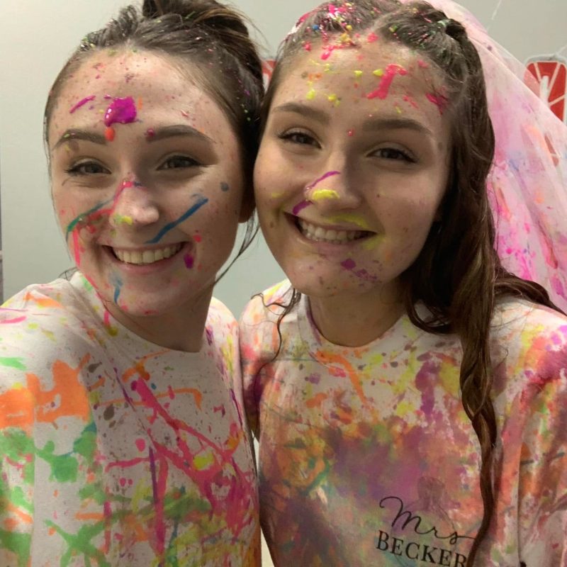 a bride wearing a veil and her friend with paint all over them