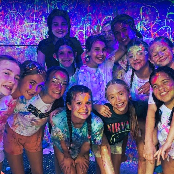 a group of people smiling with paint all over them inside of the splatter room at chaos factory