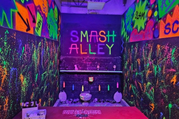 Graffiti-covered room with 'Smash Alley' neon sign, colorful splatters, and shelf with breakable items.